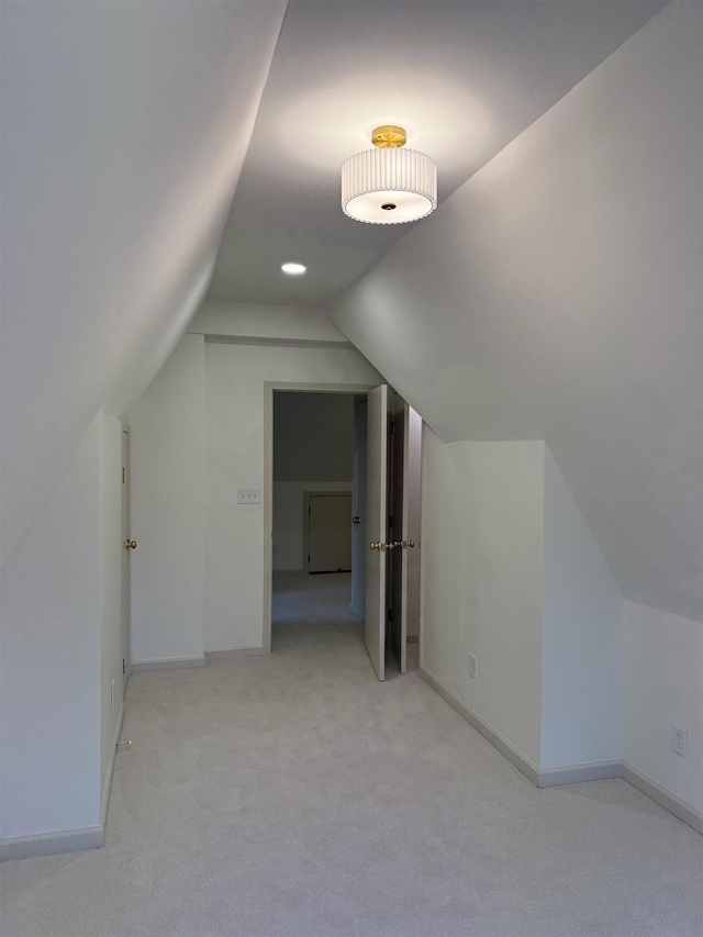 additional living space featuring light colored carpet, vaulted ceiling, and baseboards