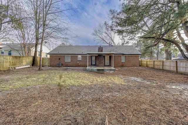 back of property featuring a fenced backyard, a chimney, cooling unit, and brick siding