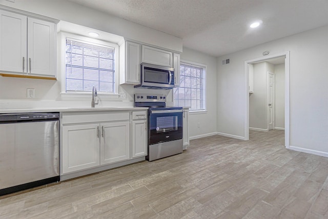 kitchen with stainless steel appliances, light countertops, light wood-style floors, white cabinetry, and a sink