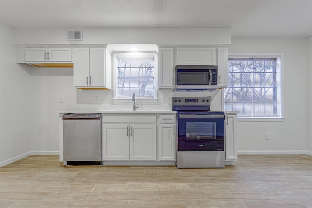 kitchen with stainless steel appliances, light countertops, a healthy amount of sunlight, a sink, and white cabinetry