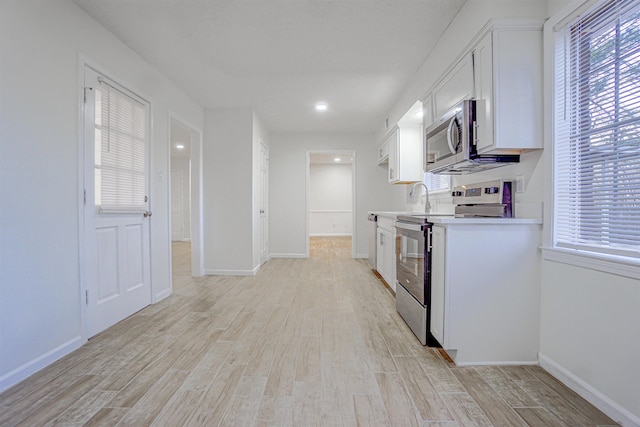 kitchen with baseboards, white cabinets, light countertops, appliances with stainless steel finishes, and light wood finished floors