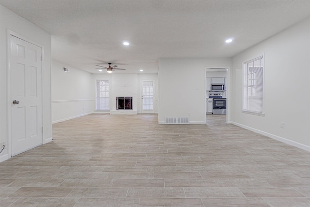 unfurnished living room featuring light wood-style floors, a fireplace, visible vents, and a ceiling fan