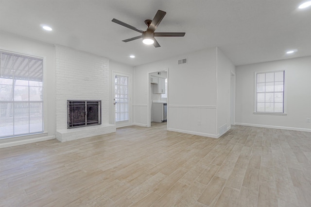 unfurnished living room with light wood-type flooring, plenty of natural light, a fireplace, and visible vents