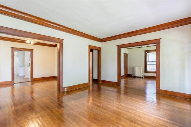 empty room featuring radiator, crown molding, baseboards, and wood finished floors