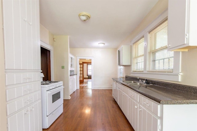 kitchen featuring dark countertops, white cabinetry, a sink, and gas range gas stove