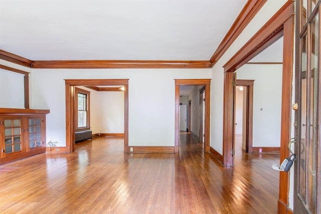 unfurnished living room featuring crown molding, baseboards, wood finished floors, and radiator