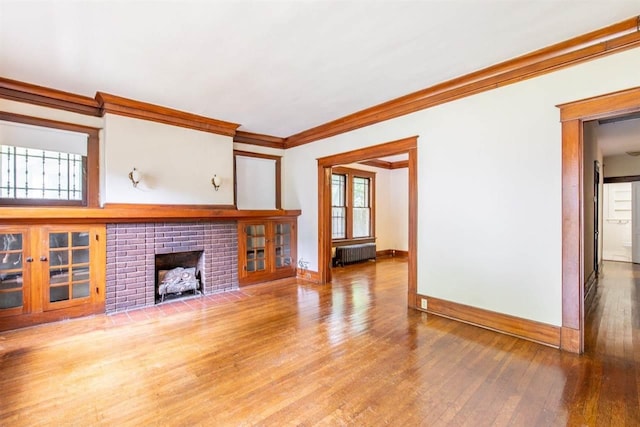 unfurnished living room featuring radiator, a brick fireplace, ornamental molding, and wood finished floors