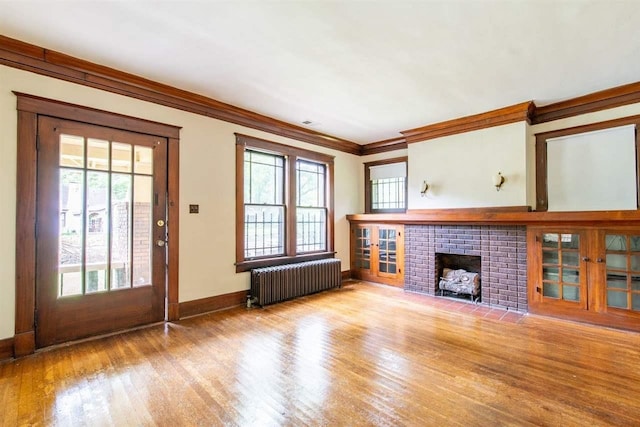 unfurnished living room with a fireplace, radiator, ornamental molding, light wood-style floors, and baseboards