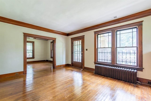 empty room featuring light wood-type flooring, radiator heating unit, visible vents, and crown molding