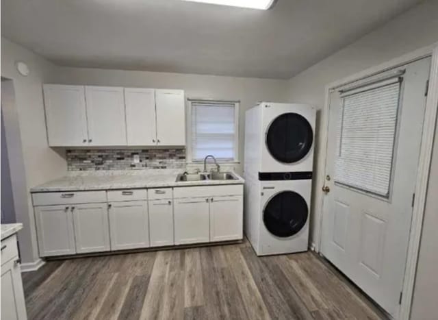 laundry room with wood finished floors, a sink, cabinet space, and stacked washer / drying machine