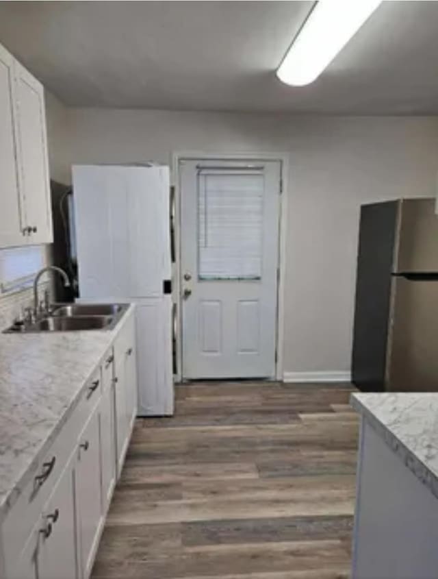 kitchen featuring dark wood-type flooring, freestanding refrigerator, white cabinetry, a sink, and baseboards