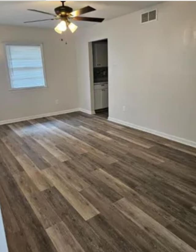 empty room with ceiling fan, dark wood-type flooring, visible vents, and baseboards