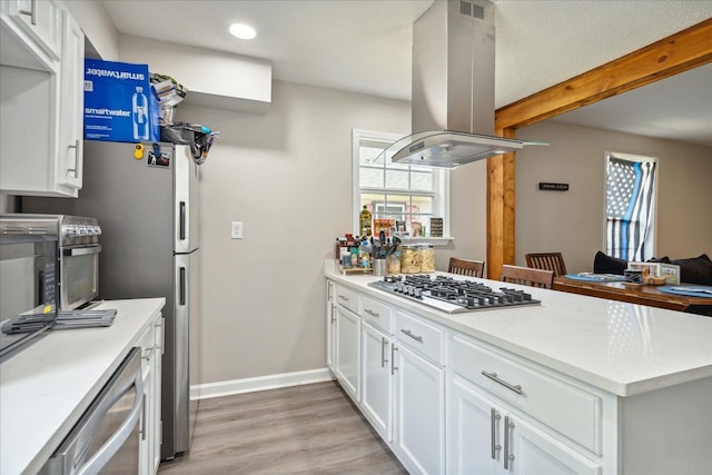 kitchen featuring white cabinets, appliances with stainless steel finishes, island exhaust hood, light countertops, and beam ceiling