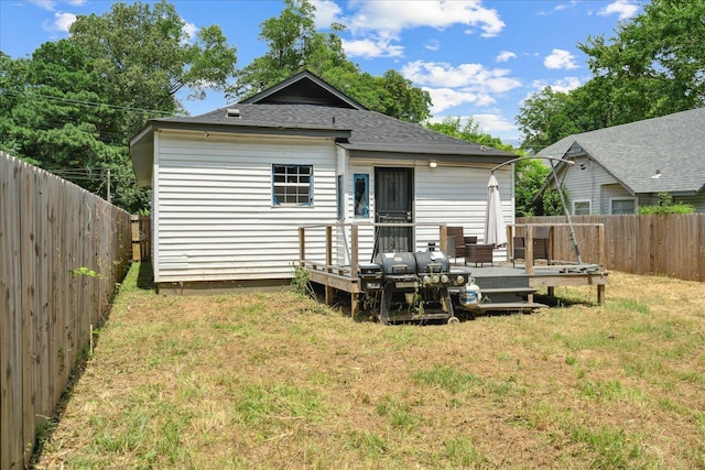 rear view of property with a deck, roof with shingles, a lawn, and a fenced backyard