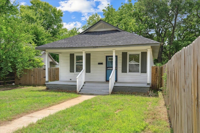 bungalow-style home with covered porch, a front lawn, a shingled roof, and fence