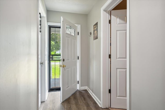 doorway to outside with a textured ceiling, dark wood finished floors, a wealth of natural light, and baseboards