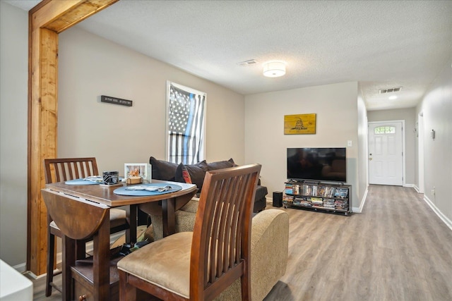 dining room with baseboards, a textured ceiling, visible vents, and wood finished floors