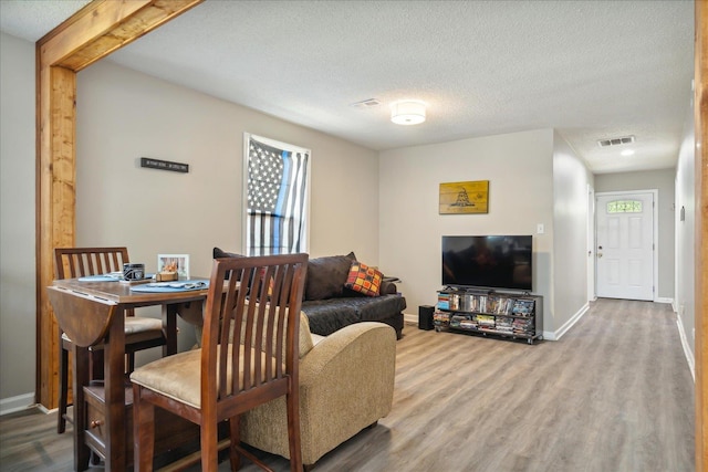 living room featuring baseboards, a textured ceiling, visible vents, and wood finished floors