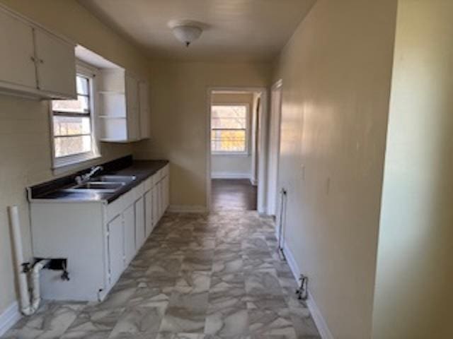 kitchen with open shelves, dark countertops, white cabinets, a sink, and baseboards