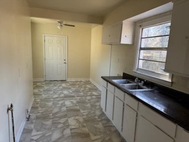 kitchen with marble finish floor, dark countertops, white cabinetry, a sink, and baseboards