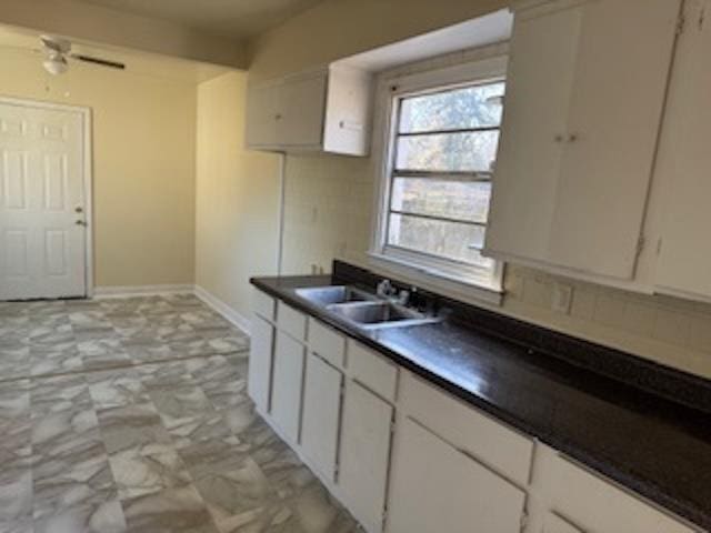 kitchen with marble finish floor, dark countertops, white cabinetry, a sink, and baseboards