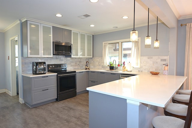 kitchen with a sink, light countertops, appliances with stainless steel finishes, hanging light fixtures, and glass insert cabinets