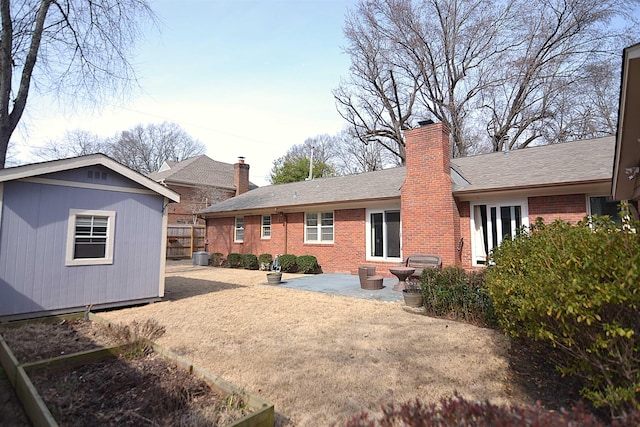 back of property featuring an outbuilding, brick siding, a chimney, and a patio area