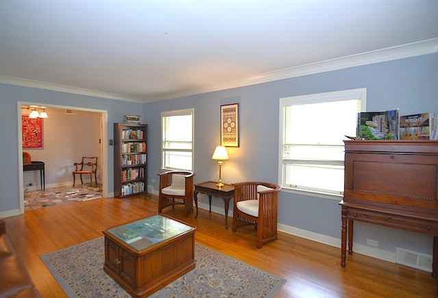 living room with ornamental molding, light wood-type flooring, visible vents, and baseboards