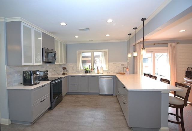 kitchen featuring stainless steel appliances, light countertops, glass insert cabinets, a peninsula, and a kitchen breakfast bar