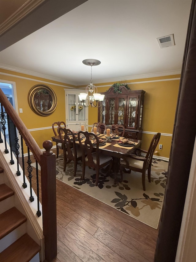 dining room with crown molding, a notable chandelier, visible vents, wood finished floors, and stairs