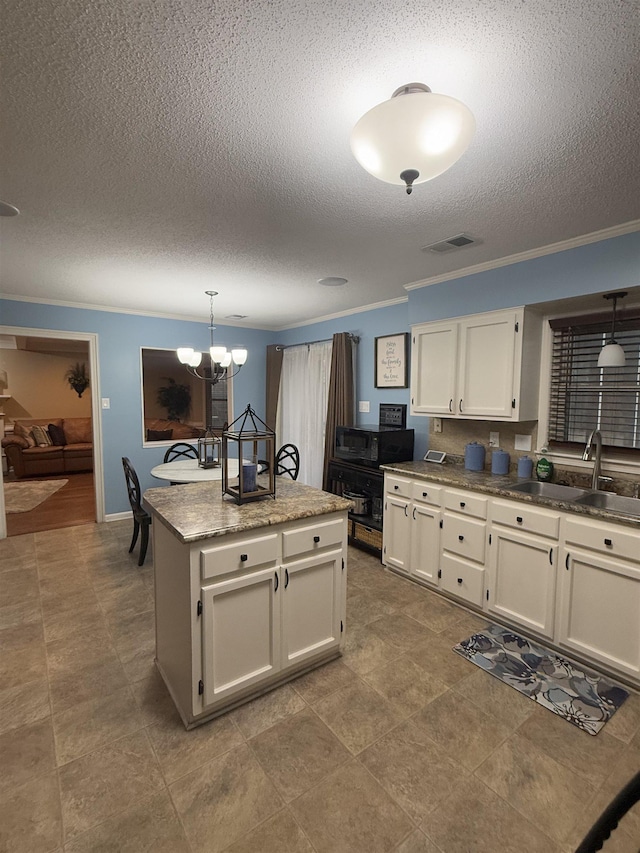 kitchen with a kitchen island, a sink, visible vents, hanging light fixtures, and ornamental molding