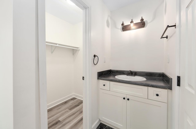 bathroom featuring a spacious closet, baseboards, wood finished floors, and vanity