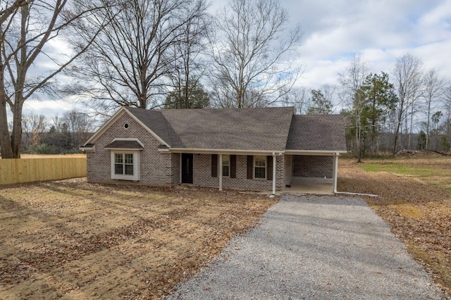 view of front of house featuring gravel driveway, brick siding, roof with shingles, fence, and an attached carport