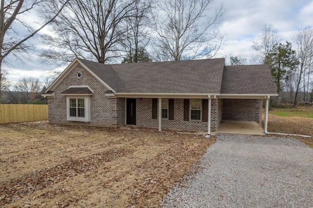 ranch-style house with an attached carport, gravel driveway, brick siding, and roof with shingles