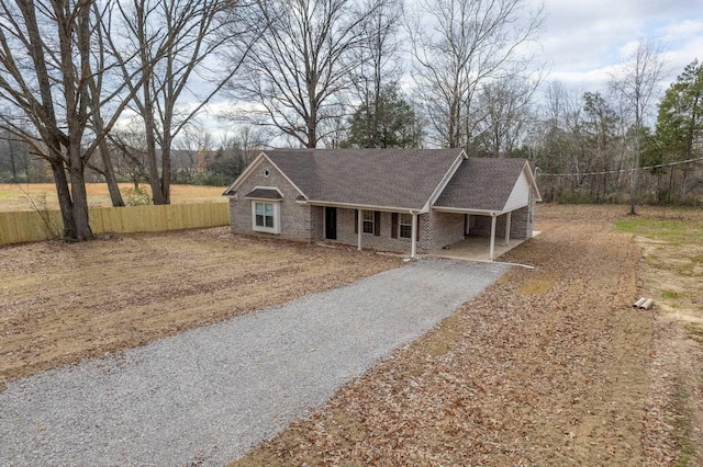 ranch-style home featuring aphalt driveway, an attached carport, roof with shingles, fence, and brick siding