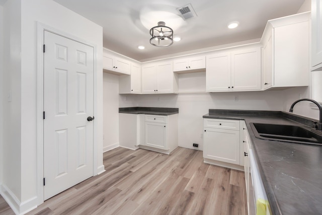 kitchen featuring dark countertops, visible vents, white cabinetry, a sink, and light wood-type flooring