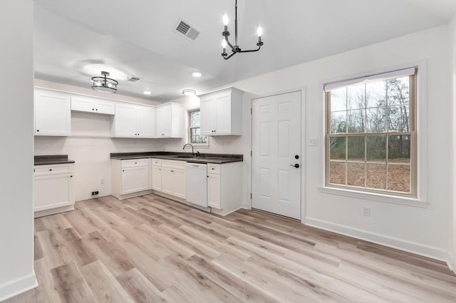 kitchen featuring dark countertops, visible vents, white cabinets, white dishwasher, and a sink