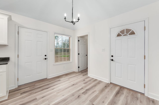 foyer entrance with light wood-type flooring, baseboards, and an inviting chandelier