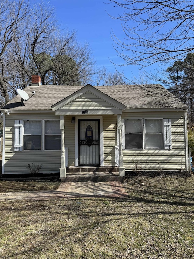 bungalow featuring a front yard, a chimney, and roof with shingles