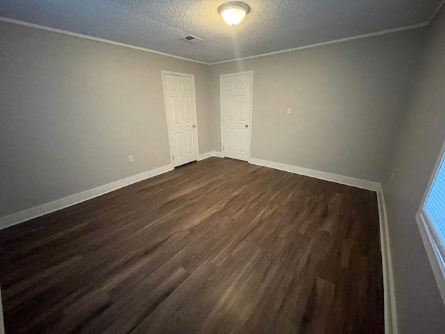 spare room featuring baseboards, visible vents, dark wood-type flooring, crown molding, and a textured ceiling