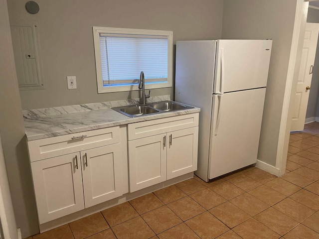 kitchen featuring light tile patterned floors, freestanding refrigerator, white cabinetry, a sink, and electric panel