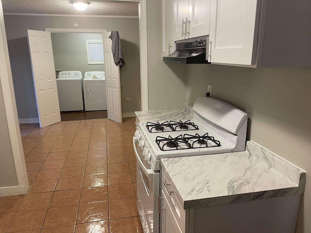 kitchen featuring white gas stove, under cabinet range hood, light countertops, ornamental molding, and independent washer and dryer