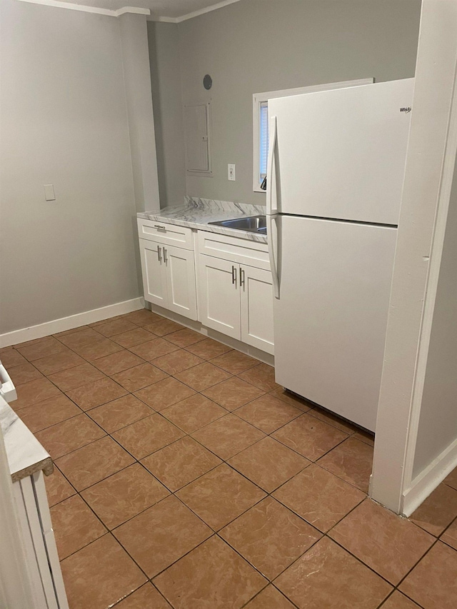 kitchen featuring light tile patterned floors, baseboards, white cabinets, freestanding refrigerator, and a sink