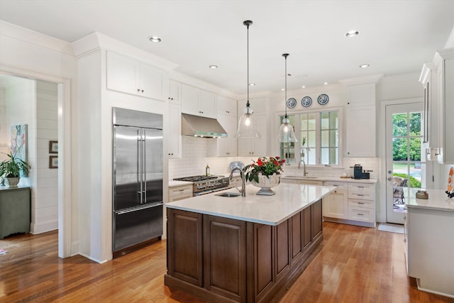 kitchen featuring an island with sink, high quality appliances, light countertops, under cabinet range hood, and pendant lighting