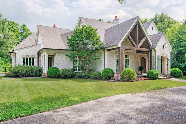 tudor home with brick siding, a chimney, a front yard, and a shingled roof