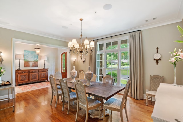 dining room with arched walkways, crown molding, visible vents, an inviting chandelier, and light wood-type flooring