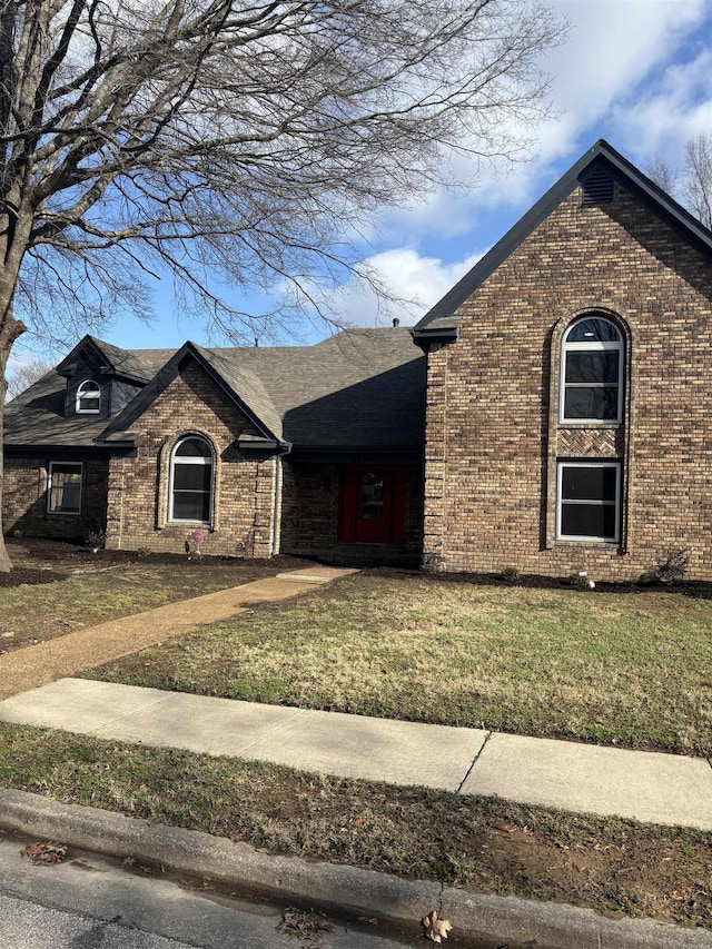 view of front of property with a shingled roof, a front yard, and brick siding