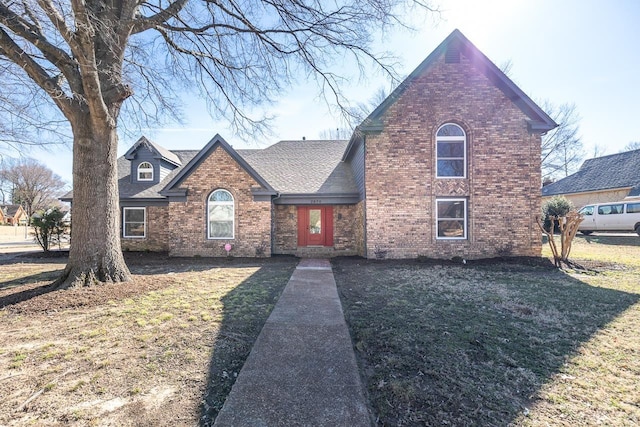 traditional-style home with brick siding, a front lawn, and roof with shingles