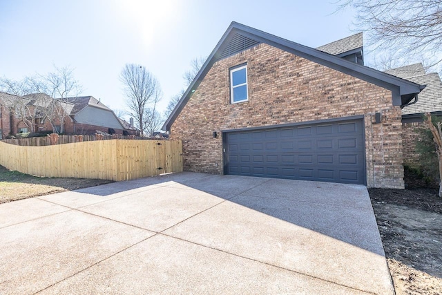 view of side of home featuring a garage, brick siding, fence, and driveway