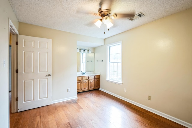 unfurnished bedroom featuring a textured ceiling, a sink, visible vents, baseboards, and light wood-type flooring